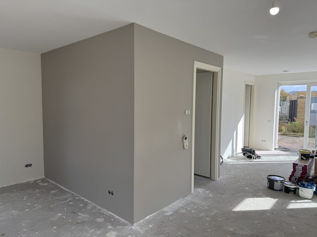 Grijs gesausde wanden rond een binnenkamer in een nieuwbouwwoning, met verfemmers op de betonvloer