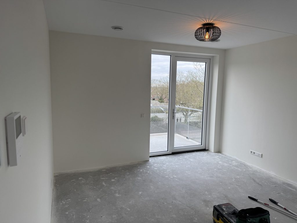 Lege kamer in een nieuw appartement met witte wanden, een glazen balkondeur en een betonvloer, klaar voor de behanger
