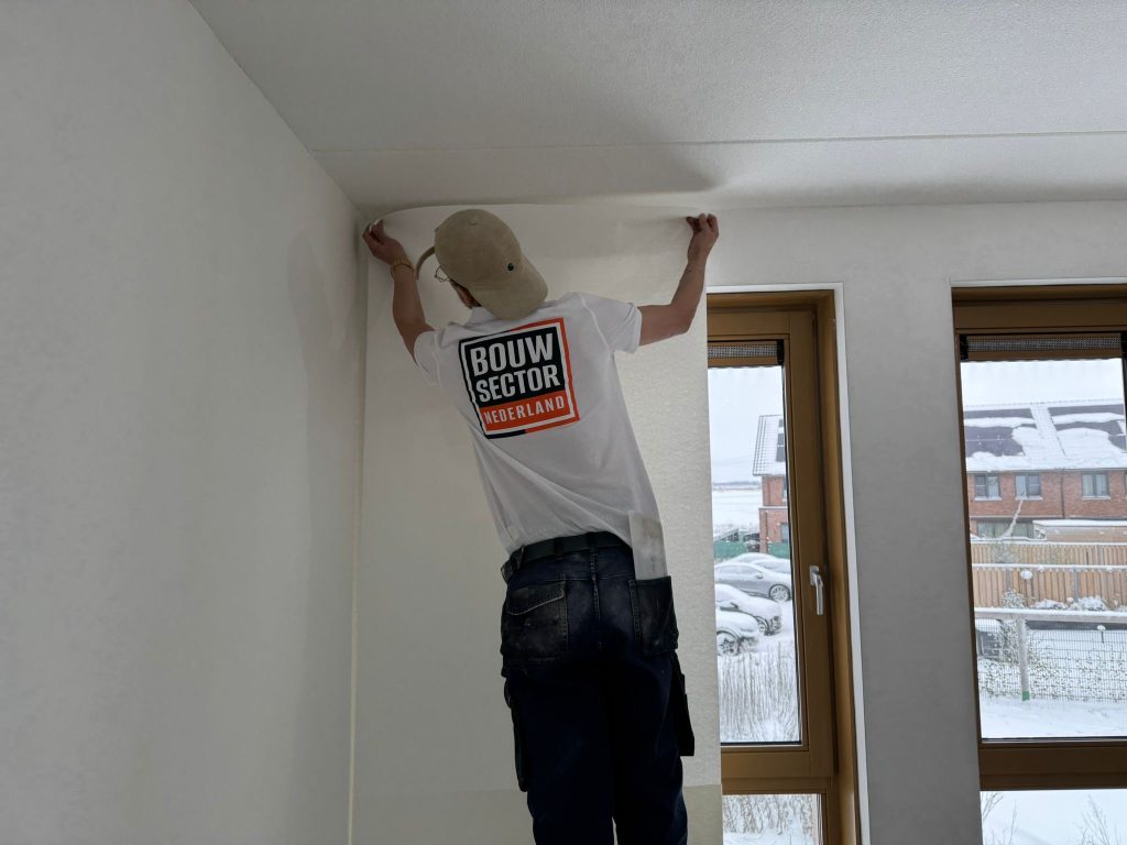 Behanger plakt een baan vlies bovenaan de muur, net onder het plafond