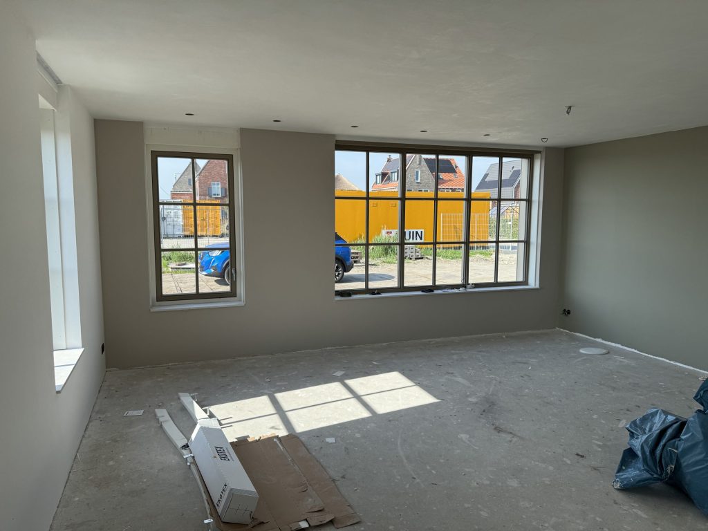 Woonkamer van een huis met strak afgewerkte, gesausde wanden en grote ramen